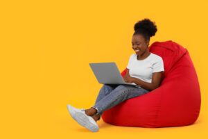 Beautiful,Young,Woman,With,Laptop,Sitting,On,Beanbag,Chair,Against
